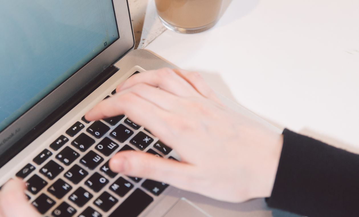 Hands typing on a laptop next to a cup of coffee during an online course