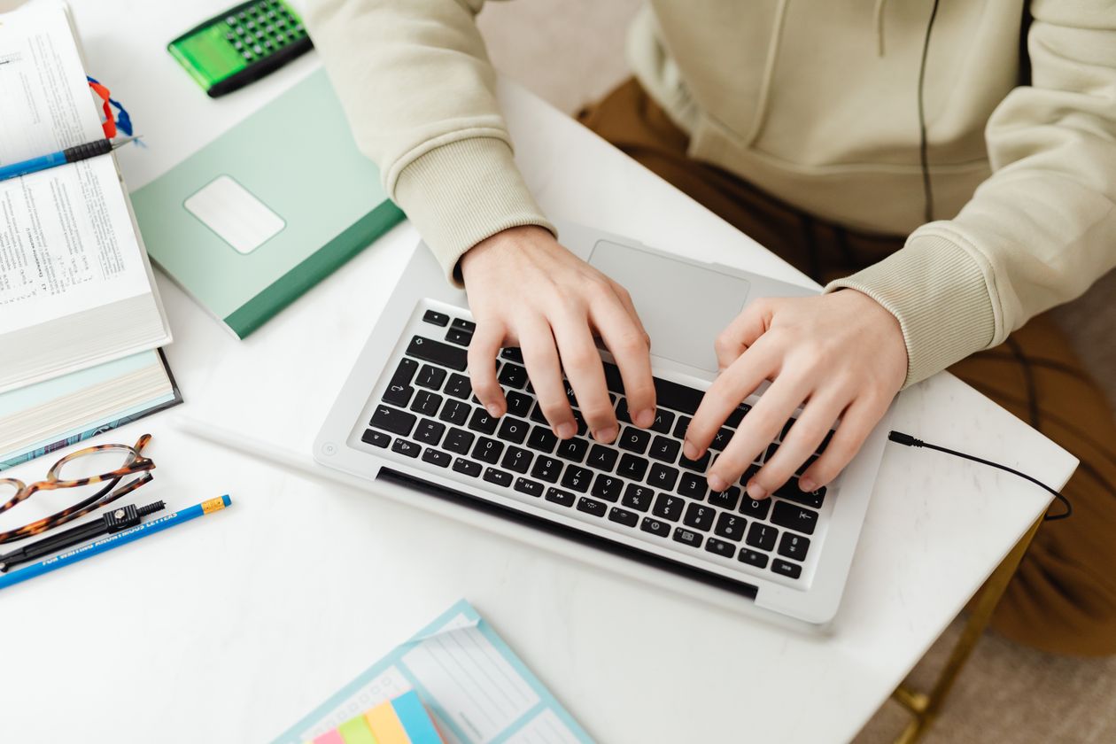 Hands typing on a laptop at a desk with study notes while taking an online AI certificate course